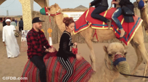A Man And Woman Are Riding A Camel In The Desert GIF