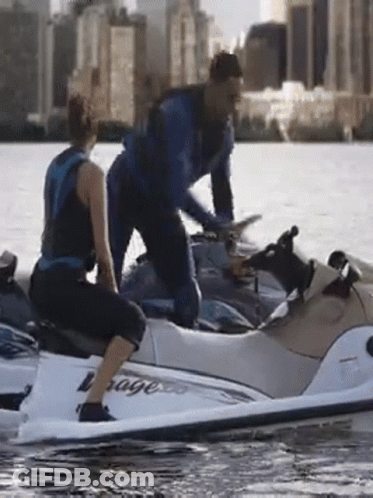 A Man And Woman Are Riding A Jet Ski That Says Voyage GIF