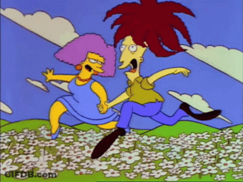 A Man And Woman Are Running Through A Field Of Flowers GIF