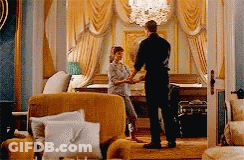A Man And Woman Are Shaking Hands In A Living Room . GIF