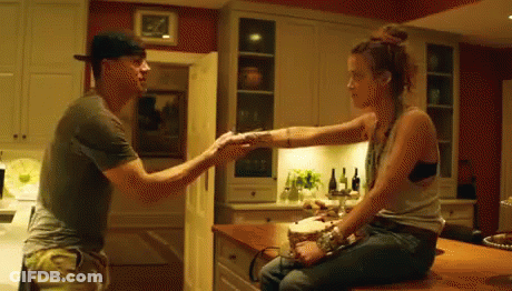 A Man And Woman Are Sitting At A Counter In A Kitchen Holding Hands . GIF