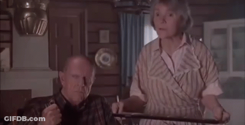A Man And Woman Are Sitting At A Table In A Living Room . GIF