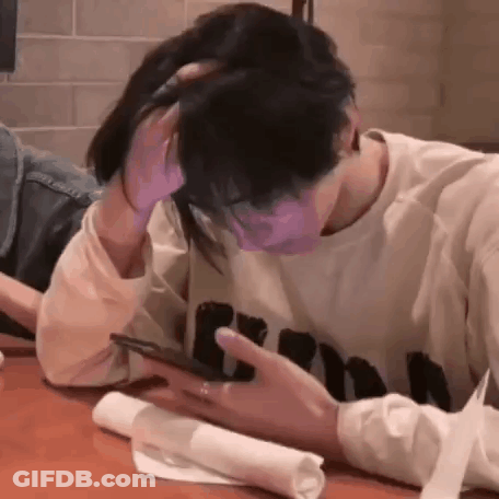 A Man And Woman Are Sitting At A Table Looking At A Cell Phone . GIF