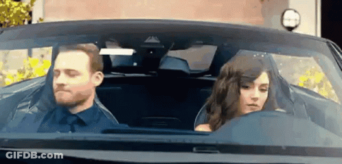 A Man And Woman Are Sitting In A Car . GIF