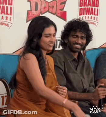 A Man And Woman Are Sitting In Front Of A Sign That Says Grand Diwali Release GIF