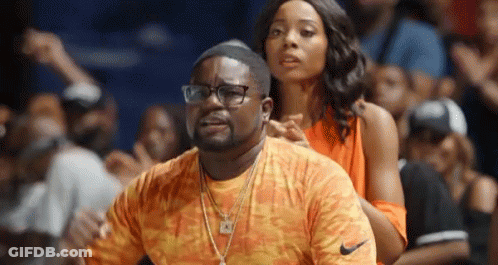 A Man And Woman Are Sitting In The Stands At A Basketball Game . The Man Is Wearing Glasses And A Nike Shirt . GIF