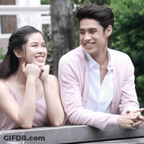 A Man And Woman Are Sitting Next To Each Other On A Bench And Smiling . GIF
