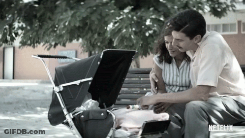 A Man And Woman Are Sitting On A Bench With A Baby In A Stroller And A Netflix Logo In The Corner GIF