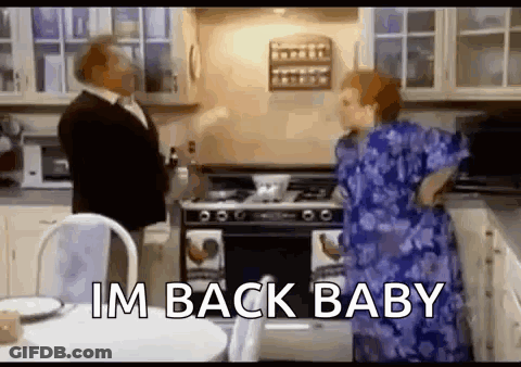 A Man And Woman Are Standing In A Kitchen With The Words `` Im Back Baby '' . GIF