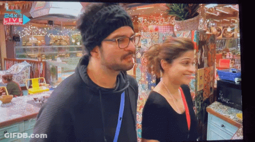 A Man And Woman Are Standing In Front Of A 24X1 Live Channel Sign GIF