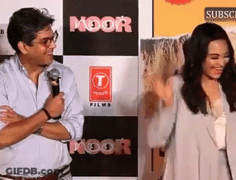 A Man And Woman Are Standing In Front Of A Sign That Says Moor Films GIF