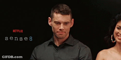 A Man And Woman Are Standing In Front Of A Sign That Says Sense 8 GIF