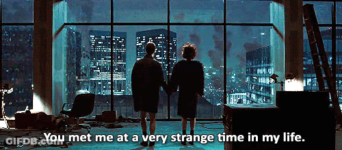 A Man And Woman Are Standing In Front Of A Window With The Words You Met Me At A Very Strange Time In My Life Below Them GIF