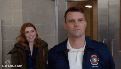 A Man And Woman Are Standing Next To Each Other In A Hallway . GIF