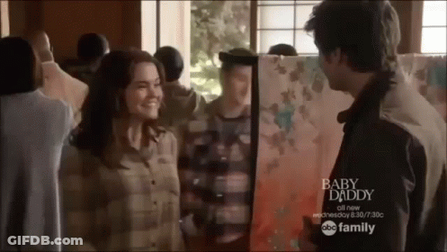 A Man And Woman Are Standing Next To Each Other In Front Of A Painting Titled Baby Daddy GIF