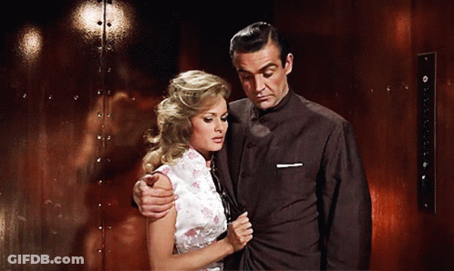 A Man And Woman Are Standing Next To Each Other In Front Of A Red Wall GIF