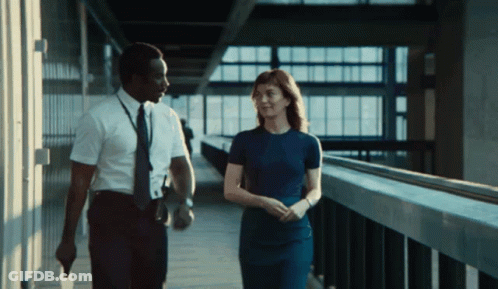 A Man And Woman Are Walking Down A Hallway GIF