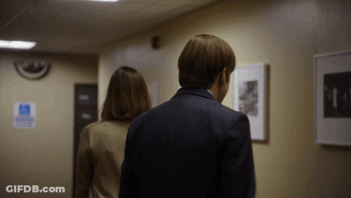A Man And Woman Are Walking Down A Hallway With A Handicap Sign On The Wall Behind Them GIF