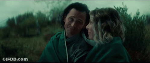 A Man And Woman Are Wrapped In A Green Blanket And Looking At Each Other GIF