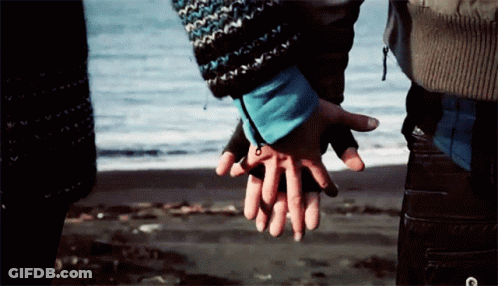 A Man And Woman Holding Hands On The Beach GIF
