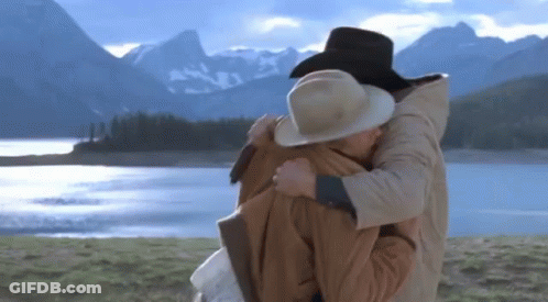 A Man And Woman Hugging In Front Of A Lake GIF