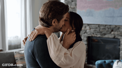 A Man And Woman Kiss In Front Of A Fireplace GIF