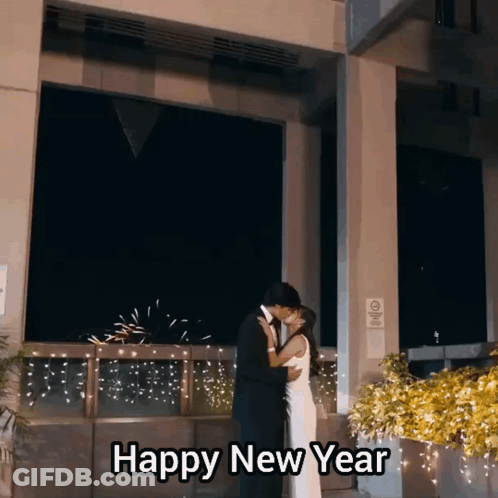 A Man And Woman Kissing In Front Of A Building With The Words Happy New Year Above Them GIF