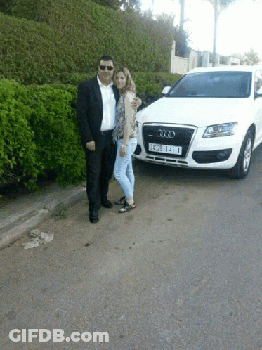 A Man And Woman Posing In Front Of An Audi GIF