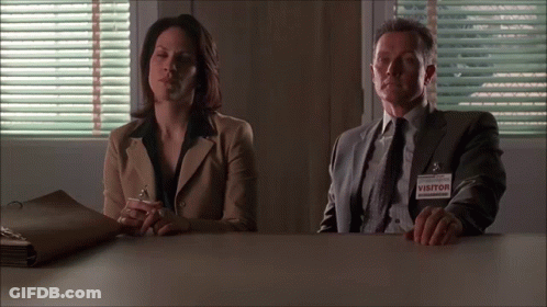 A Man And Woman Sit At A Table With A Visitor Tag GIF