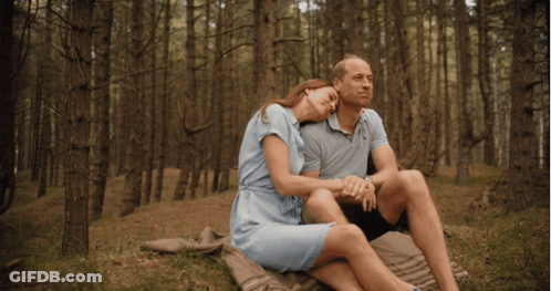 A Man And Woman Sit On A Blanket In The Woods Holding Hands GIF