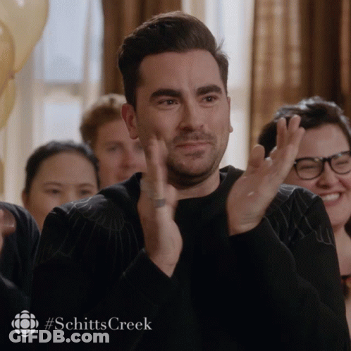 A Man Applauds With The #Schitts Creek Logo Behind Him GIF