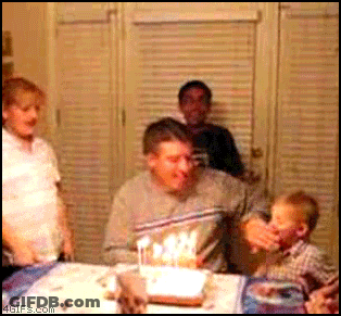 A Man Blows Out Candles On A Birthday Cake While A Child Watches GIF