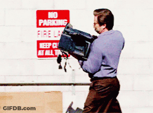 A Man Carrying A Box In Front Of A Sign That Says No Parking Fire Lane GIF