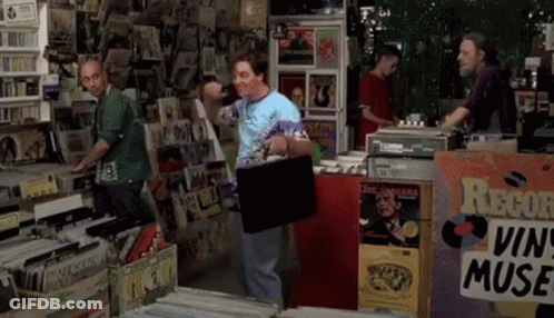 A Man Carrying A Briefcase In A Record Store GIF