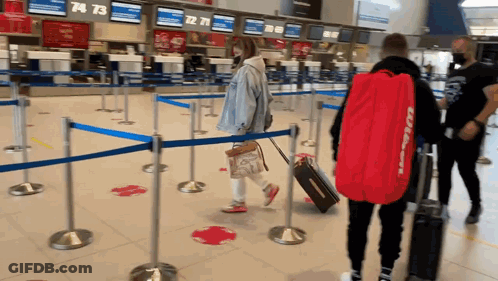 A Man Carrying A Red Bag With The Word Wilson On It Walks Through An Airport GIF