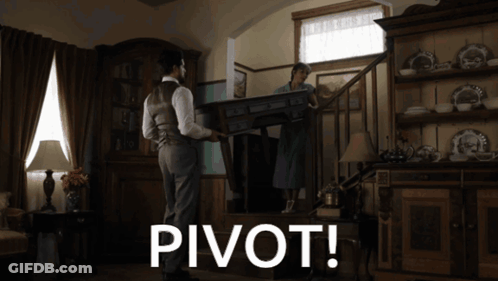 A Man Carrying A Table In A Living Room With The Word Pivot Below Him GIF