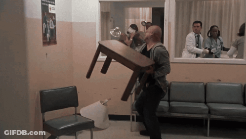 A Man Carrying A Table In A Waiting Room With A Red Cross Sign On The Wall GIF
