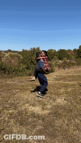 A Man Carrying A Woman In His Arms In A Field GIF