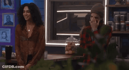 A Man Covering His Face While Standing Next To A Woman In A Plaid Shirt GIF