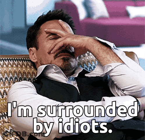 A Man Covering His Face With His Hand And The Words " I 'M Surrounded By Idiots " GIF