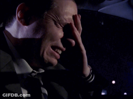 A Man Covering His Face With His Hand In A Dark Room GIF