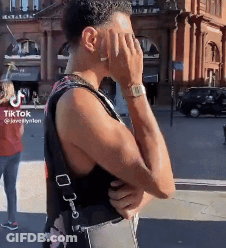 A Man Covering His Face With His Hand While Wearing A Watch And A Floral Tank Top GIF