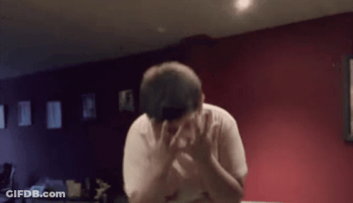 A Man Covering His Face With His Hands In A Room With Red Walls GIF