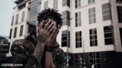 A Man Covering His Face With His Hands In Front Of A Building . GIF
