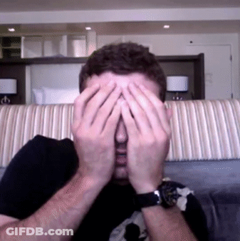 A Man Covering His Face With His Hands In Front Of A Couch GIF
