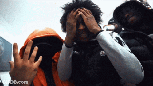 A Man Covering His Face With His Hands While Wearing An Orange Jacket GIF