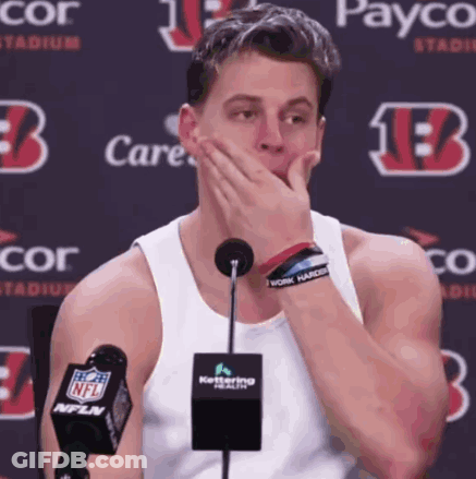 A Man Covering His Mouth While Sitting In Front Of A Microphone With A Payco Logo Behind Him GIF