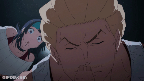A Man Covering His Mouth With His Finger While A Woman Looks On Behind Him GIF