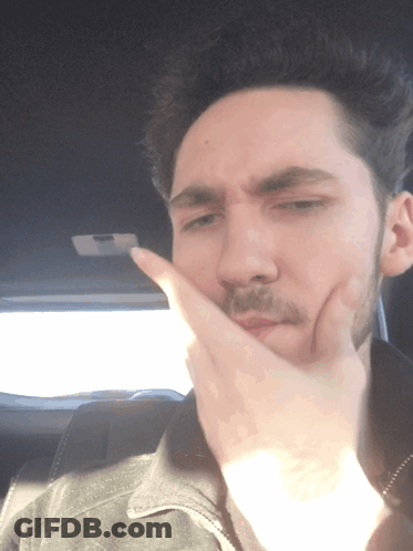A Man Covering His Mouth With His Hand While Wearing A Black Jacket GIF