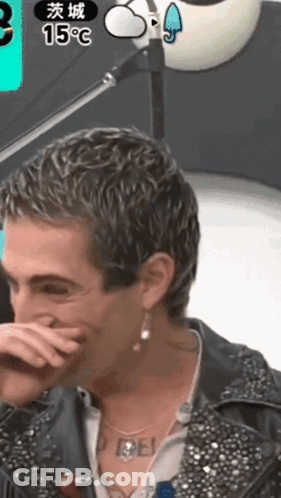 A Man Covering His Mouth With His Hand While Wearing Earrings And A Necklace That Says Rebel GIF